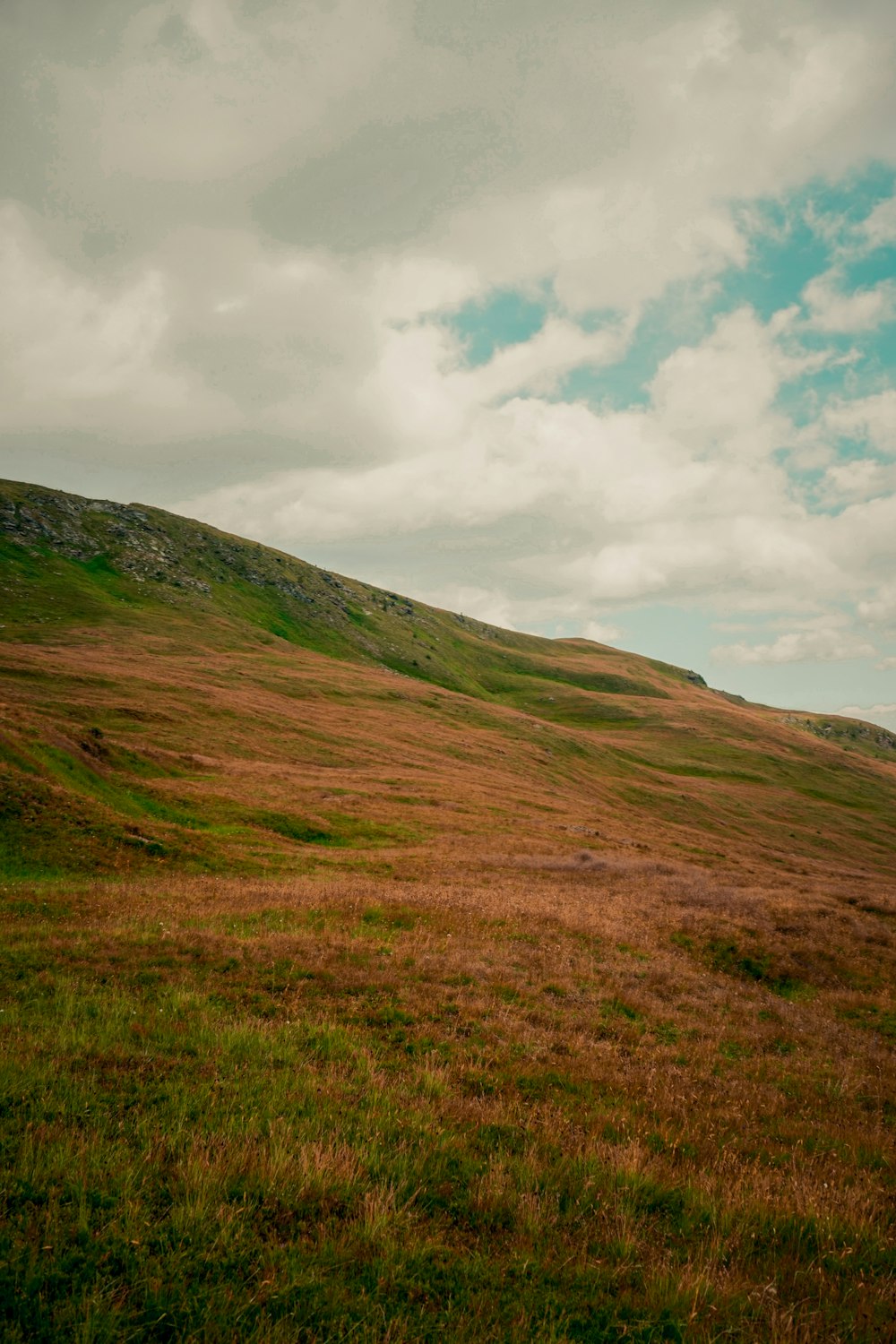 a grassy hill with clouds in the sky