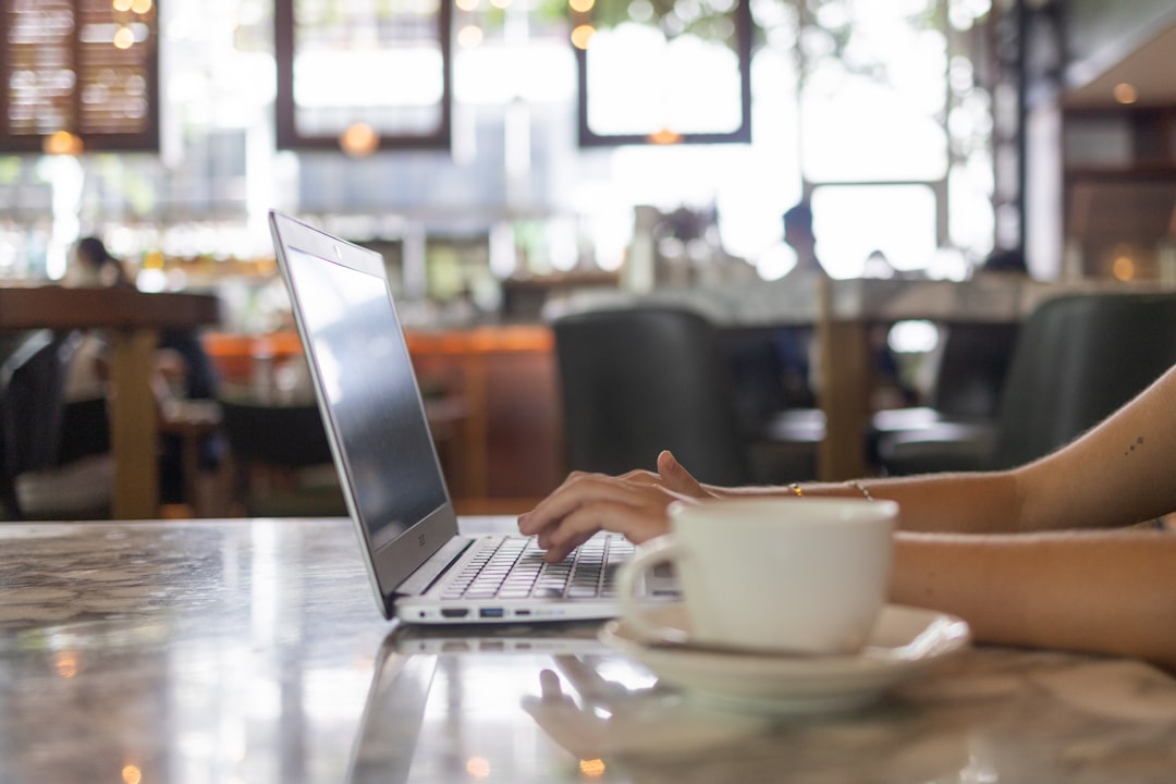 A person typing fast on a laptop in a coffee shop, morning natural light