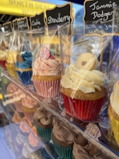Teens happily decorating cupcakes at a bustling pop-up bakery stall outdoors.