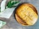 A loaf of bread with black sesame seeds rests on a wooden plate, next to large green and white variegated leaves on a textured wooden surface.