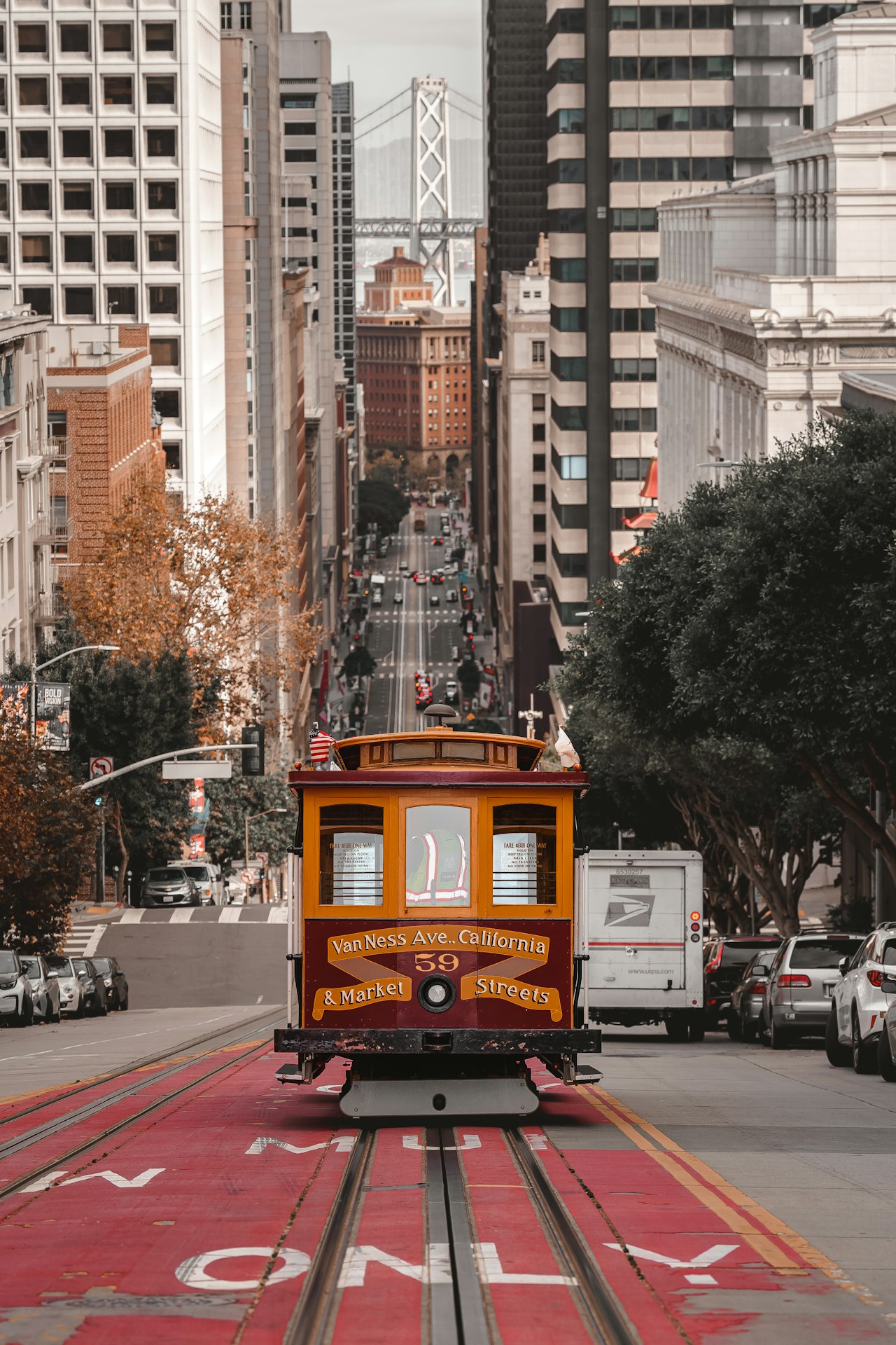 San Francisco Cable Car going down California Street with view of Bay Bridge in the background 