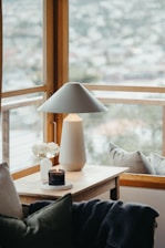 A cozy, sunlit corner featuring a plush throw blanket and a sleek, handcrafted candle on a wooden side table.