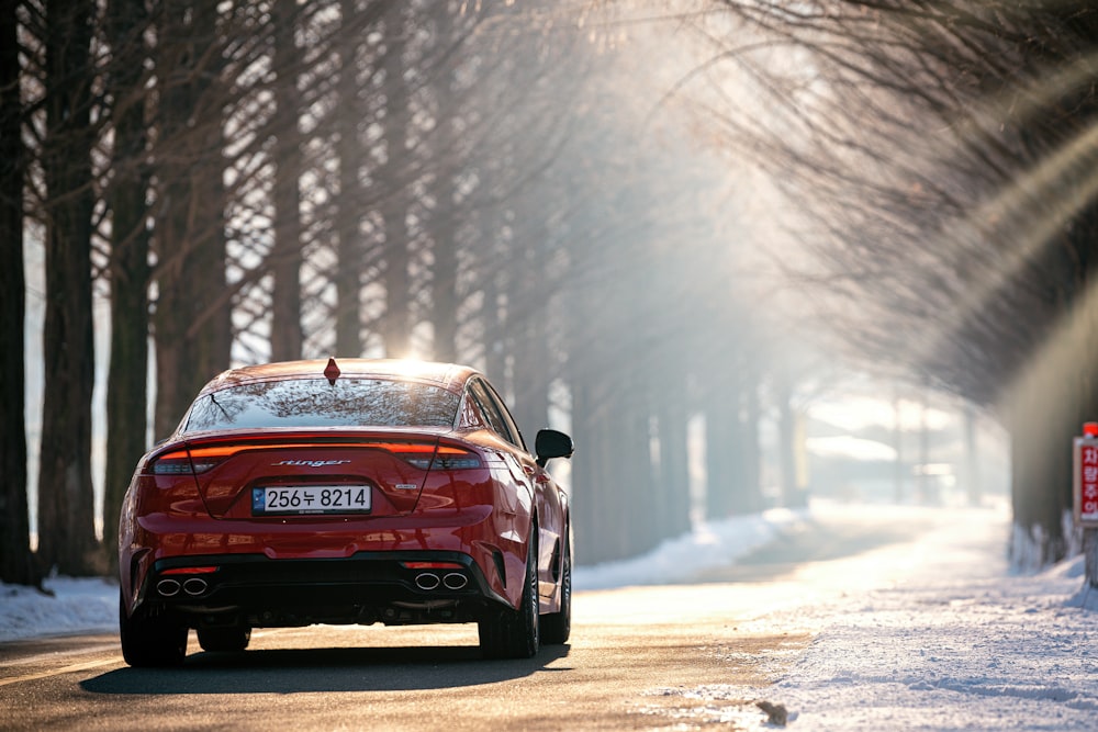 a red car driving on a road with snow on the side