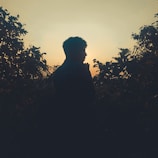 A subtle silhouette of a person standing at dawn, bathed in warm golden light.