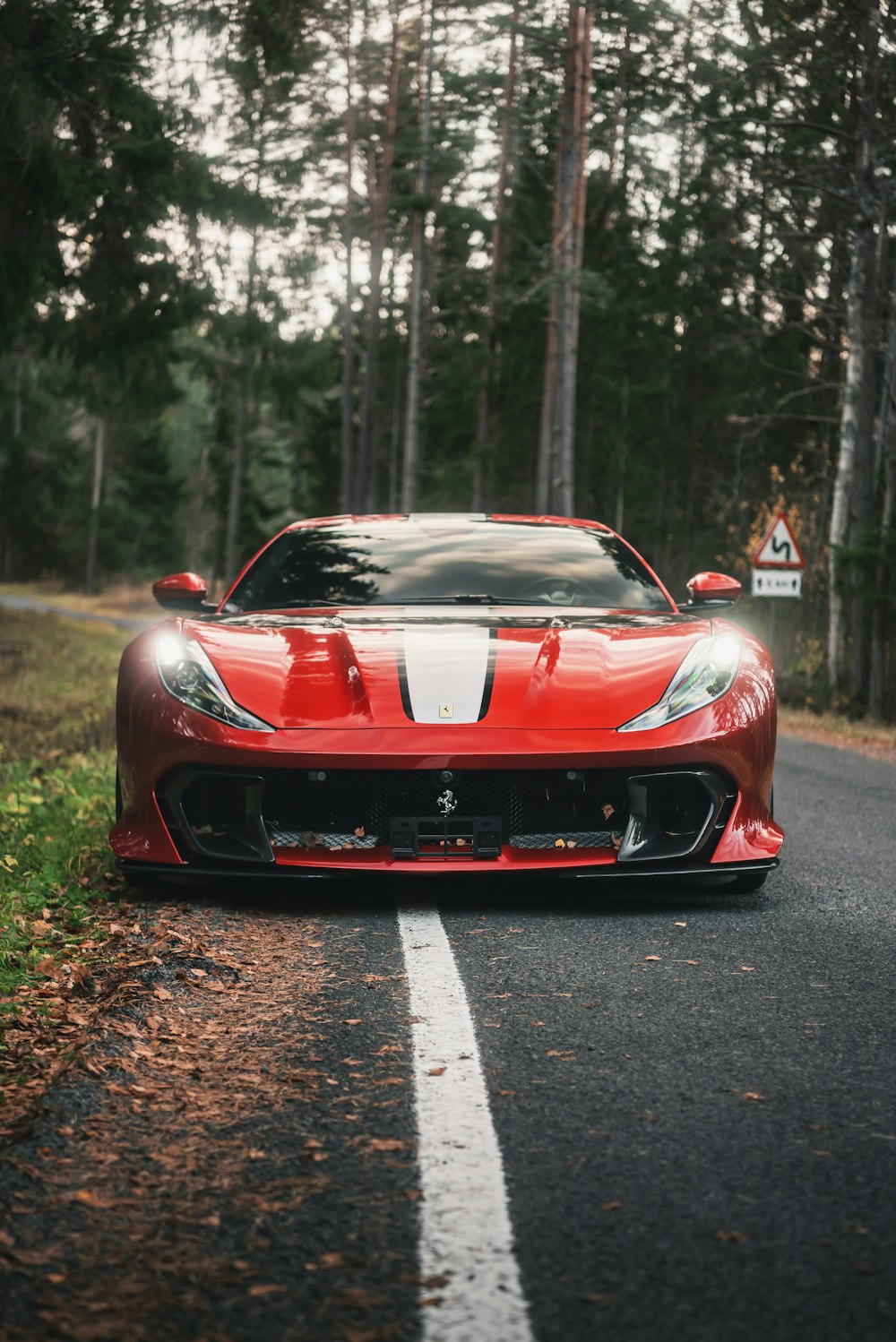 a red sports car parked in a parking lot with trees and a sign