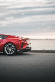 a red sports car parked on a road by a body of water