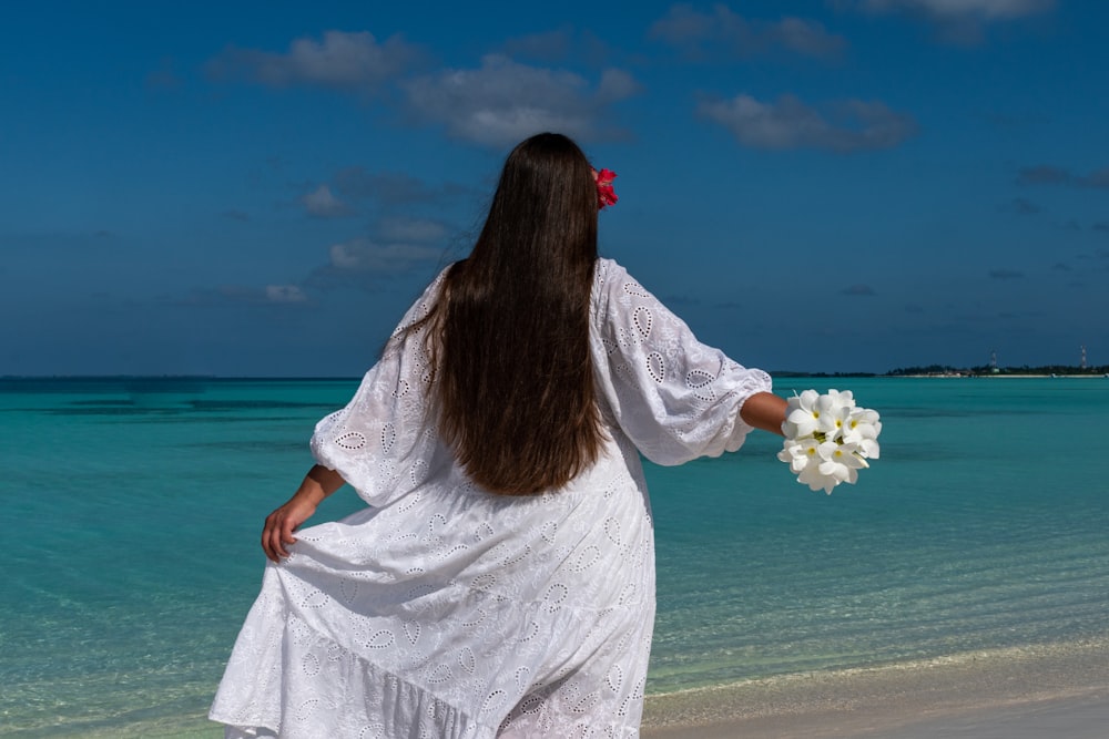 a person in a white dress holding a white flower on a beach