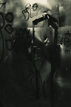 Dark graffiti-covered metal surface with abstract shapes and scribbles, creating a gritty urban atmosphere.