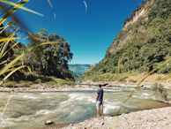 A traveler standing atop a lush green hill gazing over a winding river.