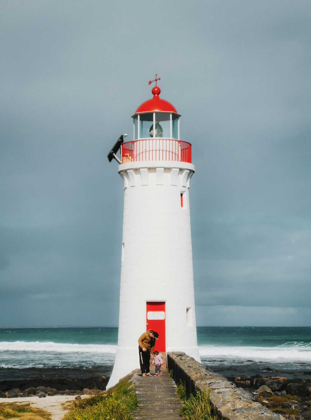 a man and a child standing on a stone walkway by a lighthouse