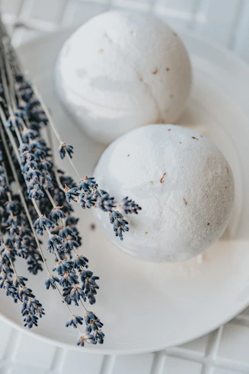 A close-up of a Moon Lavender bath bomb resting on a smooth cream surface, surrounded by delicate lavender sprigs.