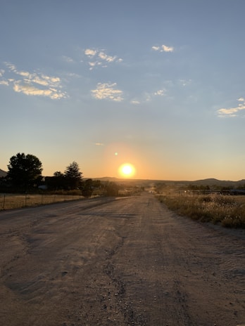 A winding dirt road cutting through golden fields under a vast blue sky at sunset.