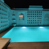 An elegant rectangular pool surrounded by white stone and subtle blue lighting at dusk.