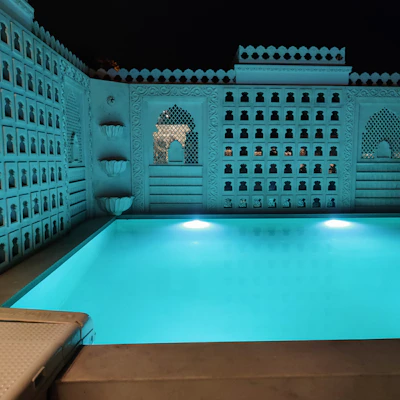 An elegant rectangular pool surrounded by white stone and subtle blue lighting at dusk.