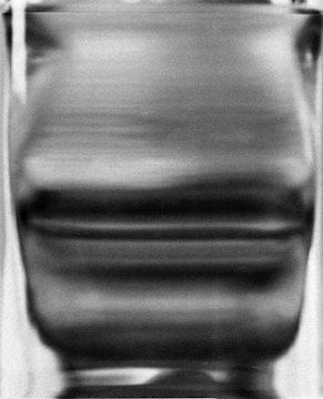 A blurred and distorted grayscale image, possibly depicting a textured or patterned surface.