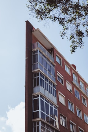 Wide shot of a multi-story commercial building made with brick and glass, surrounded by landscaping.