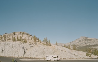 A sleek RV cruising along a scenic highway with rolling hills in the background under a clear blue sky.