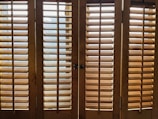 Wooden window shutters with horizontal slats allow some light to pass through, creating a pattern of shadows on the surface.