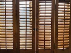 Wooden window shutters with horizontal slats allow some light to pass through, creating a pattern of shadows on the surface.
