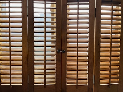 Wooden window shutters with horizontal slats allow some light to pass through, creating a pattern of shadows on the surface.