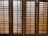 Wooden window shutters with horizontal slats allow some light to pass through, creating a pattern of shadows on the surface.