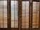 Wooden window shutters with horizontal slats allow some light to pass through, creating a pattern of shadows on the surface.