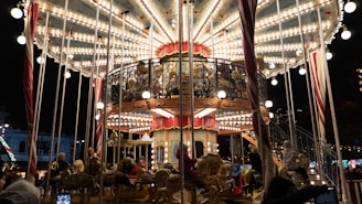 Families laughing on colorful carousel horses under glowing string lights.