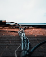 A collection of cables and wires runs vertically along a brick wall, extending towards a light sky. The wall bricks are evenly laid, with the cables neatly bundled and secured. The scene captures an urban and industrial aesthetic.