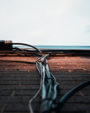 A collection of cables and wires runs vertically along a brick wall, extending towards a light sky. The wall bricks are evenly laid, with the cables neatly bundled and secured. The scene captures an urban and industrial aesthetic.