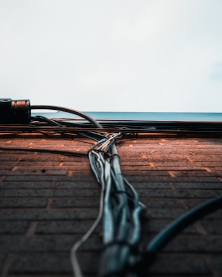 A collection of cables and wires runs vertically along a brick wall, extending towards a light sky. The wall bricks are evenly laid, with the cables neatly bundled and secured. The scene captures an urban and industrial aesthetic.