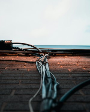 A collection of cables and wires runs vertically along a brick wall, extending towards a light sky. The wall bricks are evenly laid, with the cables neatly bundled and secured. The scene captures an urban and industrial aesthetic.