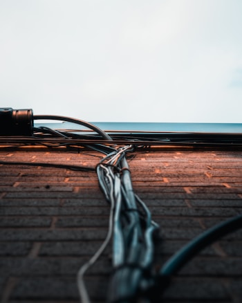 A collection of cables and wires runs vertically along a brick wall, extending towards a light sky. The wall bricks are evenly laid, with the cables neatly bundled and secured. The scene captures an urban and industrial aesthetic.