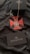 A silver necklace with a geometric pendant is placed on a black fabric featuring a red cross-like design. A black box with a white design is positioned above the necklace. A black card with the word 'SUBURBIA' in white letters and a logo is also visible.