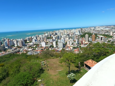 A panoramic view of a coastal city with green parks and modern buildings under a clear sky.