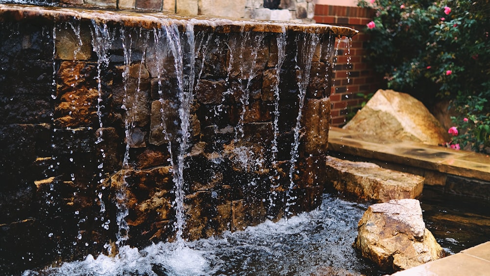 a water fall in a garden with rocks and flowers