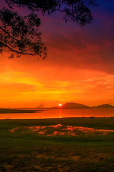 A vibrant sunset over Lake Reschen with the iconic submerged church tower rising from the water.