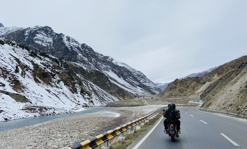 a man riding a motorcycle down a road next to a mountain