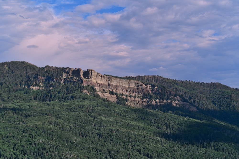 a mountain with a forest below it under a cloudy sky