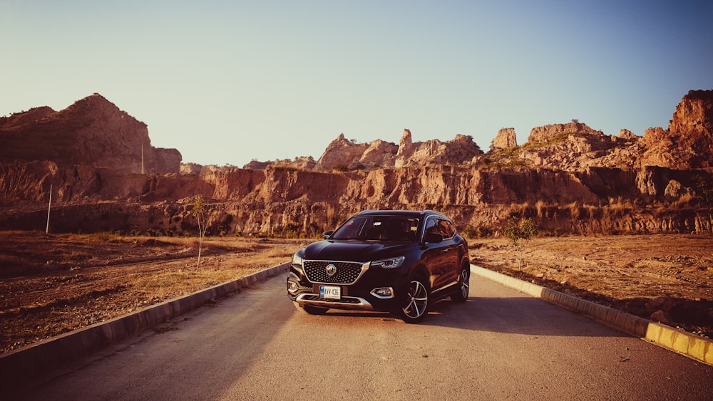 a black car driving down a road next to mountains