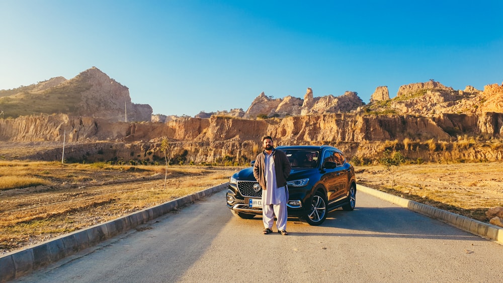 a man standing next to a car on a road