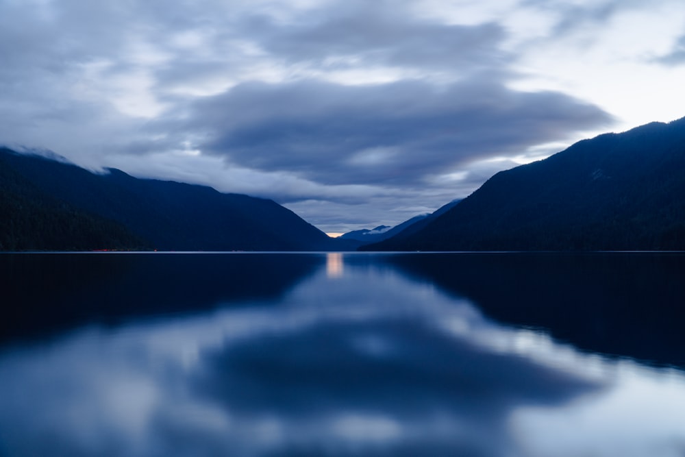 a body of water surrounded by mountains under a cloudy sky