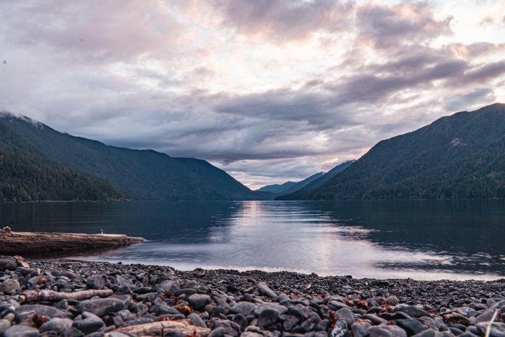 a body of water surrounded by mountains under a cloudy sky