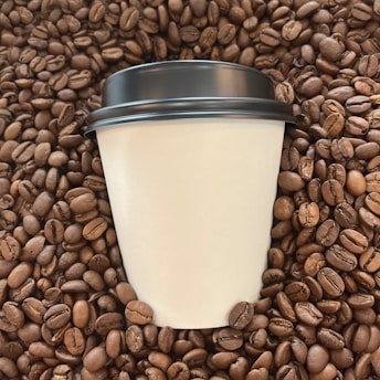 A disposable coffee cup with a black lid is surrounded by a large number of roasted coffee beans.