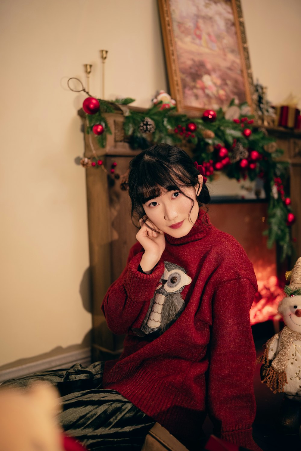 a woman sitting in front of a fireplace wearing a red sweater
