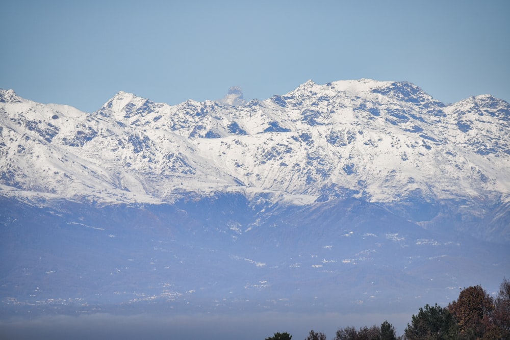 a snow covered mountain range with trees in the foreground