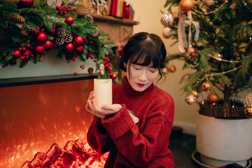 a woman in a red sweater holding a cup in front of a fireplace