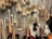 A variety of cleaning brushes hanging on a metal perforated wall. The brushes vary in shape, size, and bristle type, including long-handled brushes, round scrubbers, and small handheld brushes. The materials range from wooden handles to metal wire loops, and bristle colors are primarily beige, white, and brown.