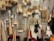 A variety of cleaning brushes hanging on a metal perforated wall. The brushes vary in shape, size, and bristle type, including long-handled brushes, round scrubbers, and small handheld brushes. The materials range from wooden handles to metal wire loops, and bristle colors are primarily beige, white, and brown.