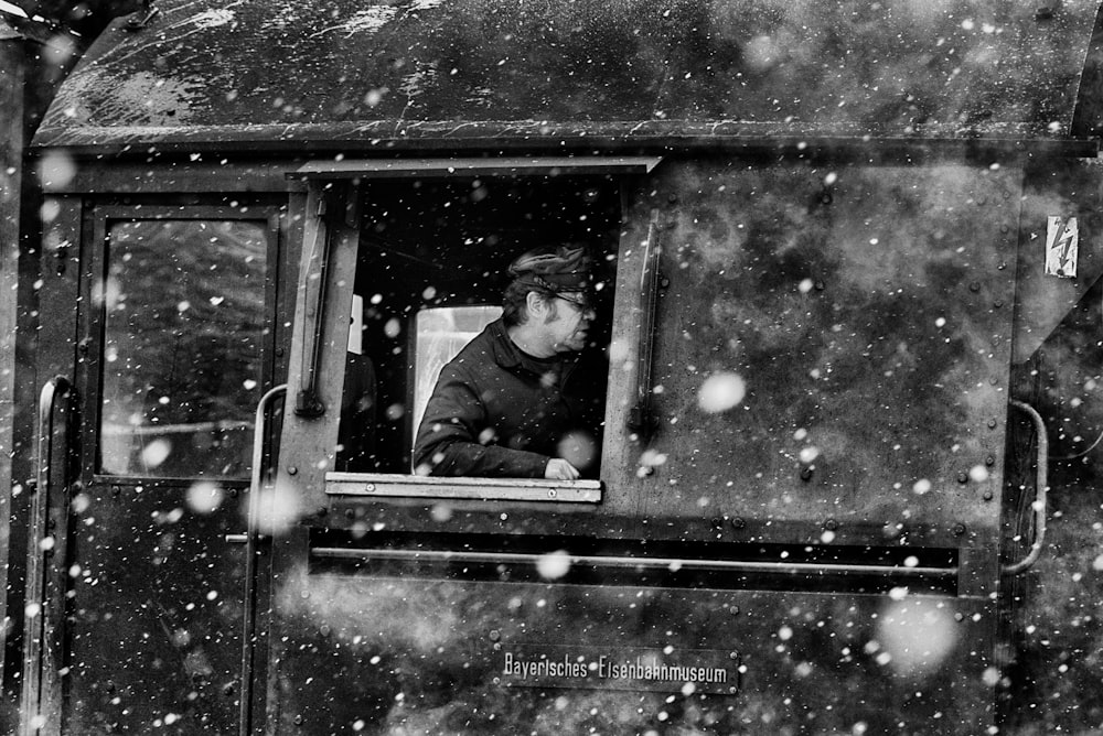 a black and white photo of a man looking out of a train window