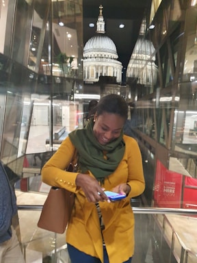 A stylish woman smiling while holding a smartphone in a bright, modern setting.